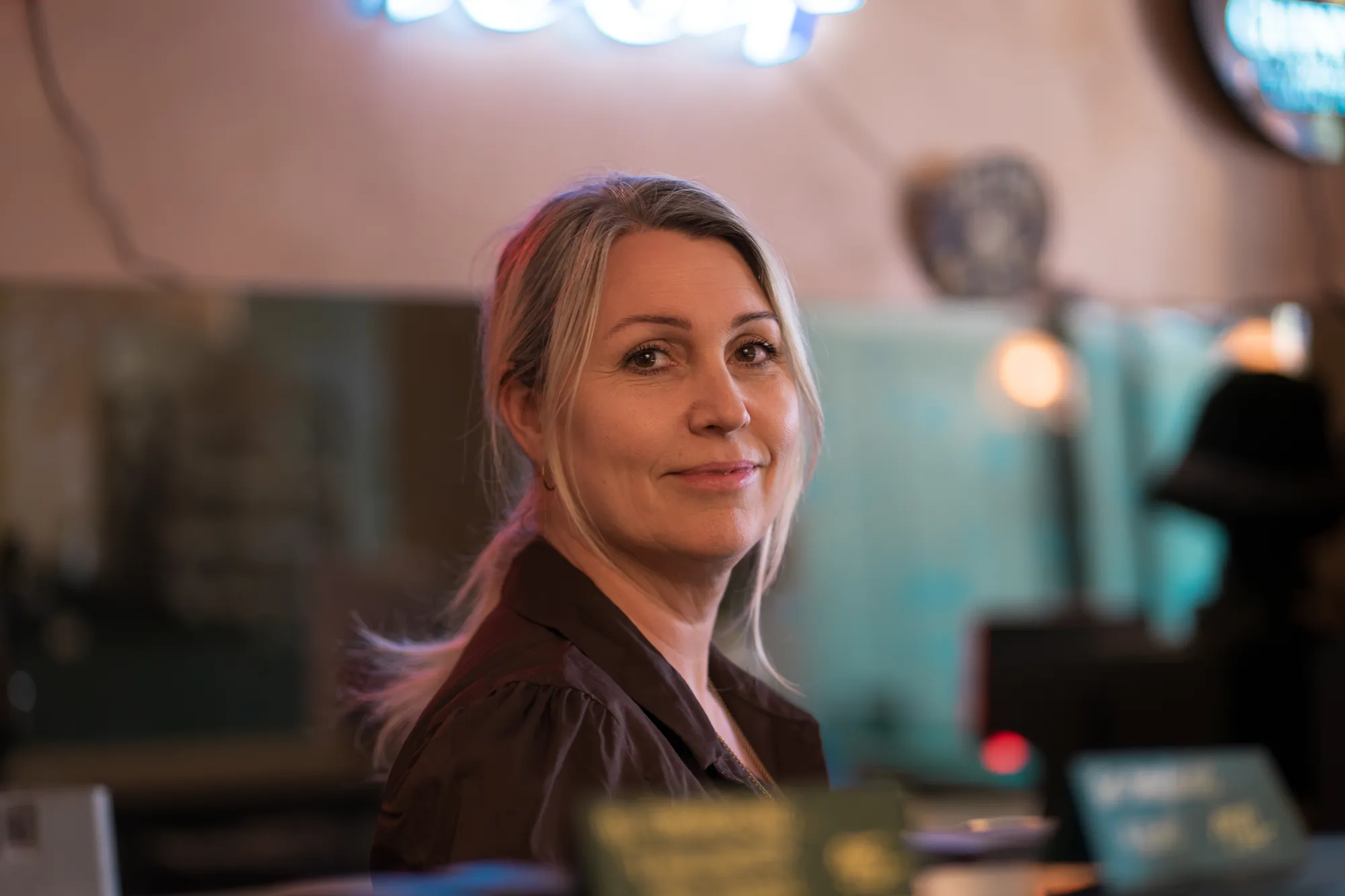 Portræt af Britta Højen Holm ved en bar med neonlys