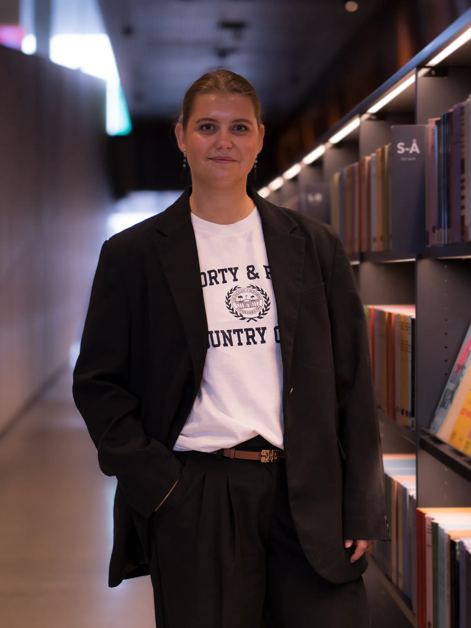 Portræt af Mathilde i sort jakkesæt mellem bogreoler