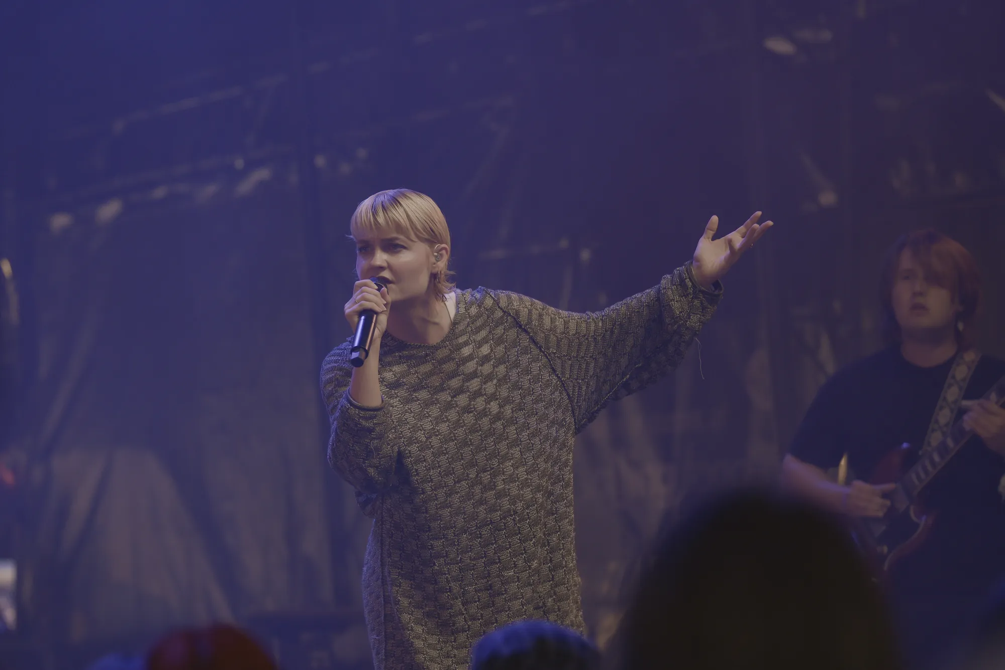 Sangerinde med mikrofon og band på scenen i blåt lys